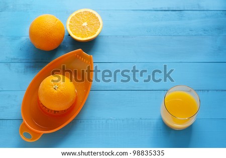 glass of orange juice and squeezed orange against blue table top