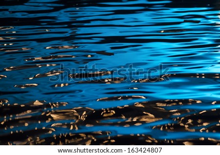 A horizontal photographic image of ripples on top of a body of water with blue reflections