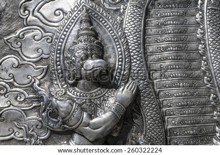 A horizontal photographic image of an ancient metal wall sculpture from Wat Srisuphan Temple in Chiang Mai Thailand depicting a part human part bird being