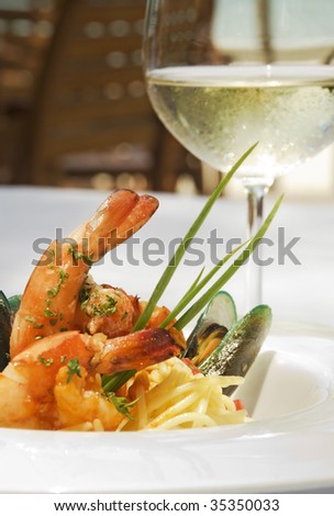 Shrimp and oyster spaghetti served in a white ceramic plate and accompanied with a glass of a white wine.