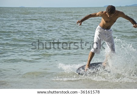 A young man skin boarding at the beach on a sunny day.