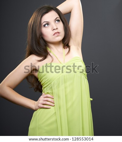 Attractive young woman in a green dress. Woman raised her hand. Looks to the upper-left corner. On a gray background