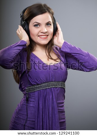 Attractive young woman in a lilac dress. Woman listening to music on headphones. On a gray background