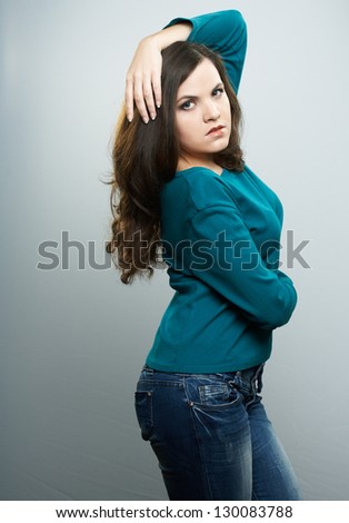 Attractive young woman in a blue shirt and jeans. Woman holds her hand over her head. On a gray background