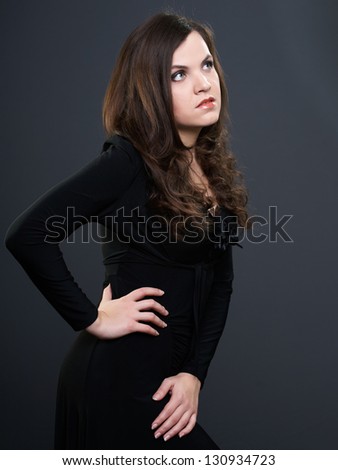 Attractive young woman in a black dress. Woman looking to the left. On a gray background