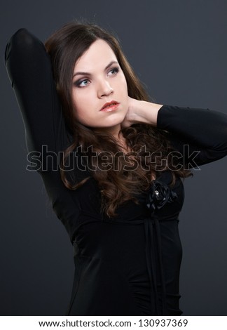 Attractive young woman in a black dress. Woman raised one arm and looking to the left. On a gray background