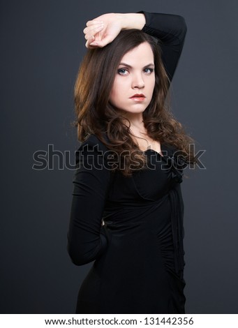 Attractive young woman in a black dress. Woman holding one hand over her head. On a gray background
