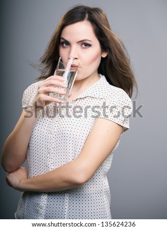 Attractive young woman in a white blouse. Woman drinks mineral water. On a gray background