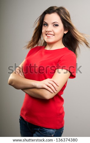 Attractive young woman in a red shirt. Woman standing with folded hands. Hair in motion. On a gray background