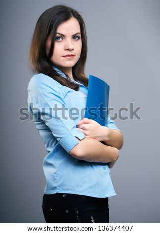 Attractive young woman in a blue blouse. Woman holds a blue folder. On a gray background
