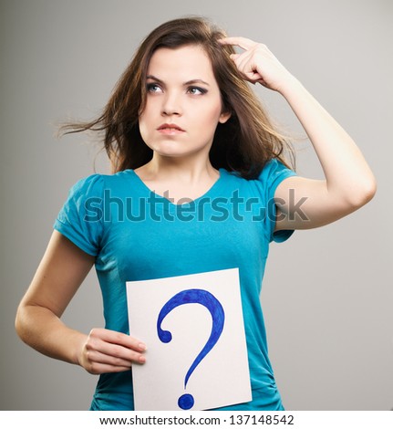 Attractive young woman in a blue shirt. Woman holds a poster with a big question mark. Thinks. On a gray background