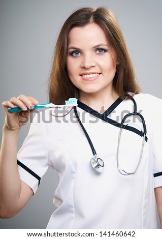 Attractive young nurse. Woman holding a toothbrush with toothpaste. Isolated on a gray background