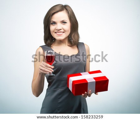 Attractive young woman in a gray business dress. Holding red gift box and glass of wine. On a gray background