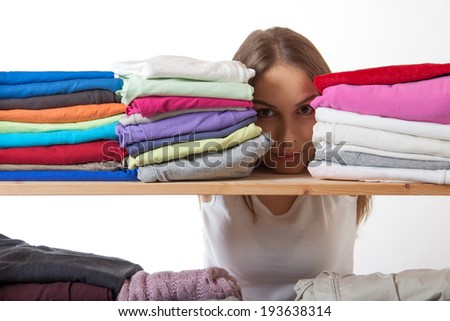 young woman hiding behind a shelf with clothing, isolated on white background