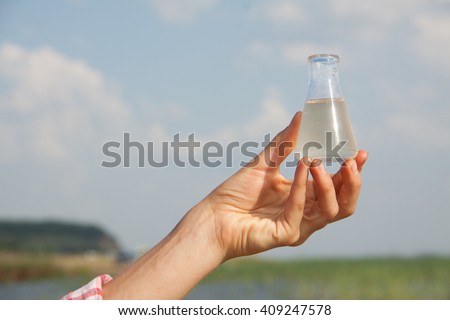 Water Purity Test. Hand holding a chemical flask with water, lake or river in the background.
