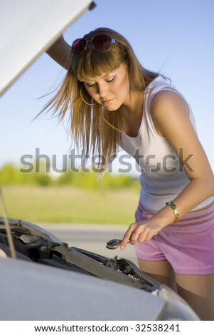 Beautiful blonde girl looking under the hood of the car