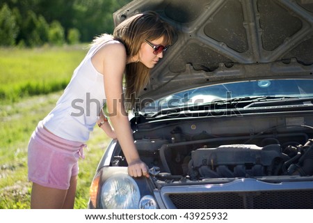 Beautiful blonde girl looking under the hood of the car