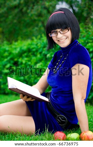 Young beautiful woman in glasses on green field with apple and book