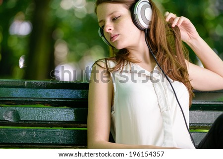 Woman listening to music. Female student girl outside in park listening to music on the headphones