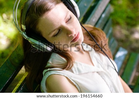 Woman listening to music. Female student girl outside in park listening to the music on the headphones