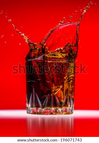 Glass with whiskey splash on red background