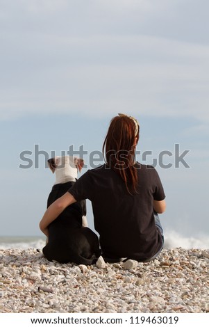 beautiful young woman embracing her dog looking at the sea