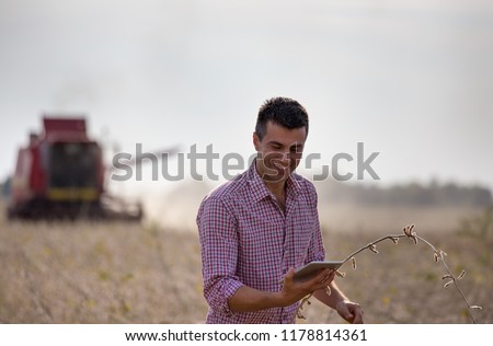 Happy farmer with tablet standing in soybean field during harvest