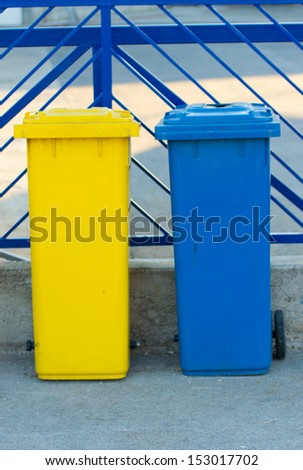Yellow and blue trash can and blue metal fence in background