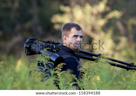 Photographer holds photo camera and stand on his shoulder in forest
