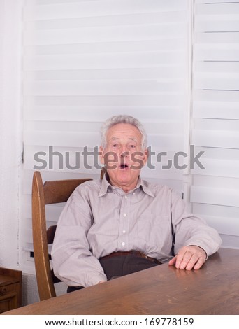 Surprised old man sitting at dining table