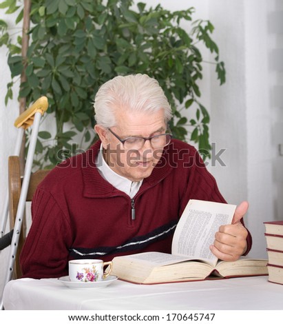 Older man with walking stick sitting in his home and reading books