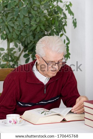 Older man reading herbal book in his home