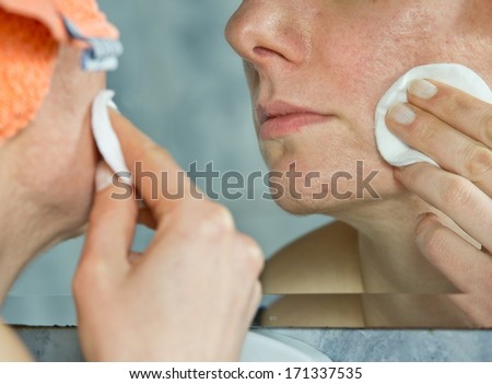 Girl with problematic skin cleansing face with cotton swab in front of mirror in bathroom