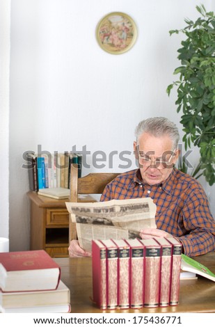 Senior man reading old newspaper from archive in his library