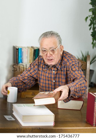 Old man with reading glasses and books in his library