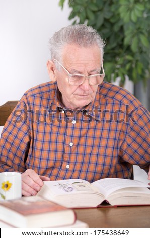 Old man with reading glasses reading book in dining room