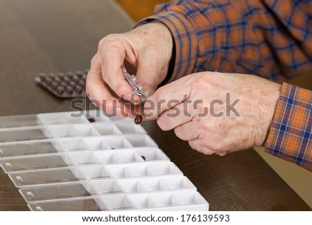 Old man taking out pills from blister into pills box to organize weekly dose