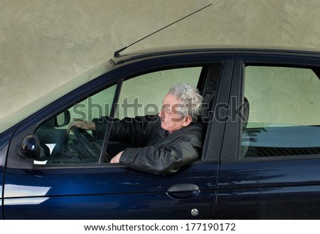 Old man driving car and holds elbow out on opened window