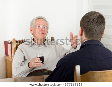 Old man with glass of wine in hand explaining something to young man