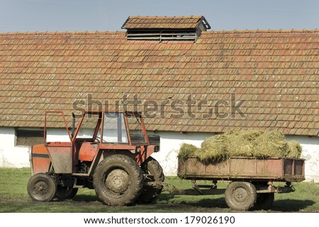 Muddy tractor with hay in trailer in front of stable