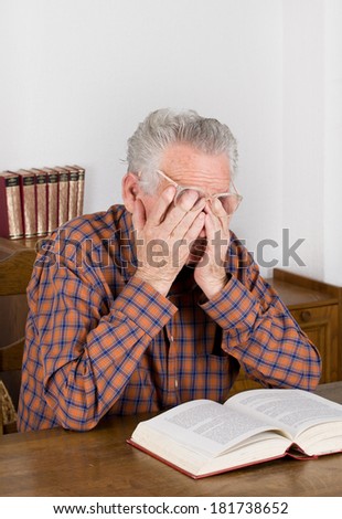 Tired old man holding hands on eyes after reading a book