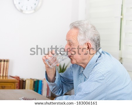 Old man in pajamas drinking glass of water and have pills blister on table