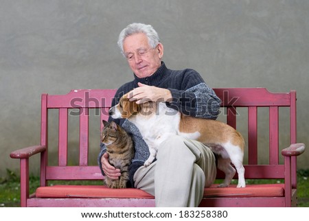 Senior man cuddles dog and cat on his lap on bench