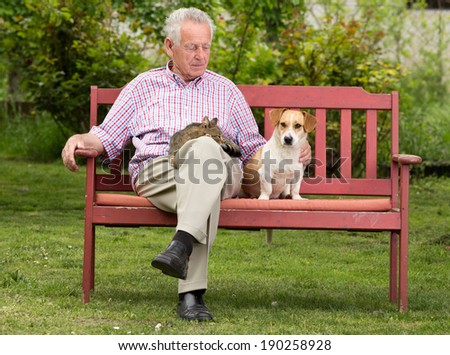Old man resting on bench and cuddling dog and cat