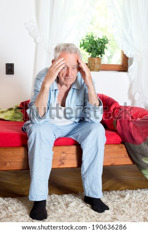 Old man sitting on bed and holding head with hands