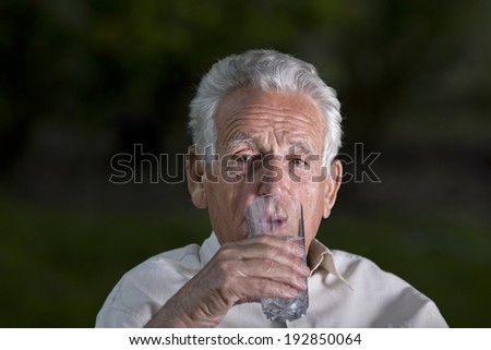 Old man drinking water from big glass in garden