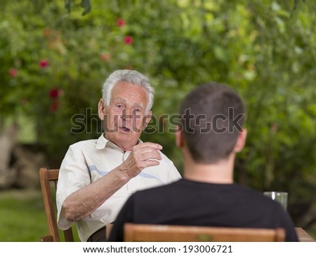 Serious old man talking with grandson and explaining by hand