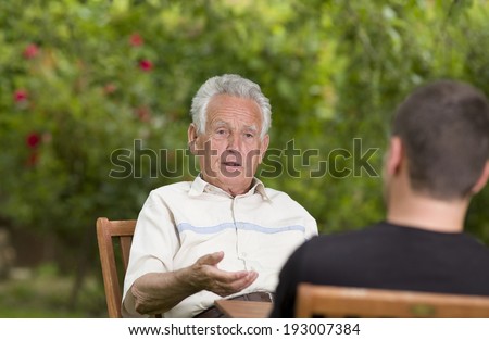 Serious old man talking with grandson and explaining by hand