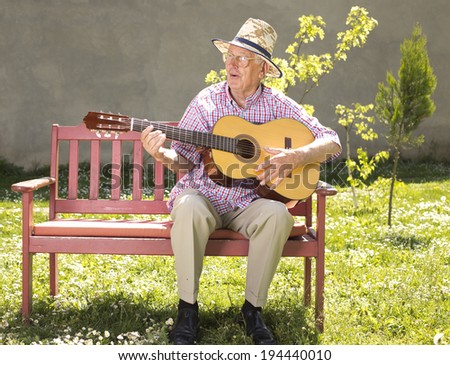 Old man with straw hat playing acoustic guitar on bench