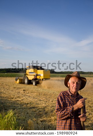 Old peasant standing on field with combine in background
